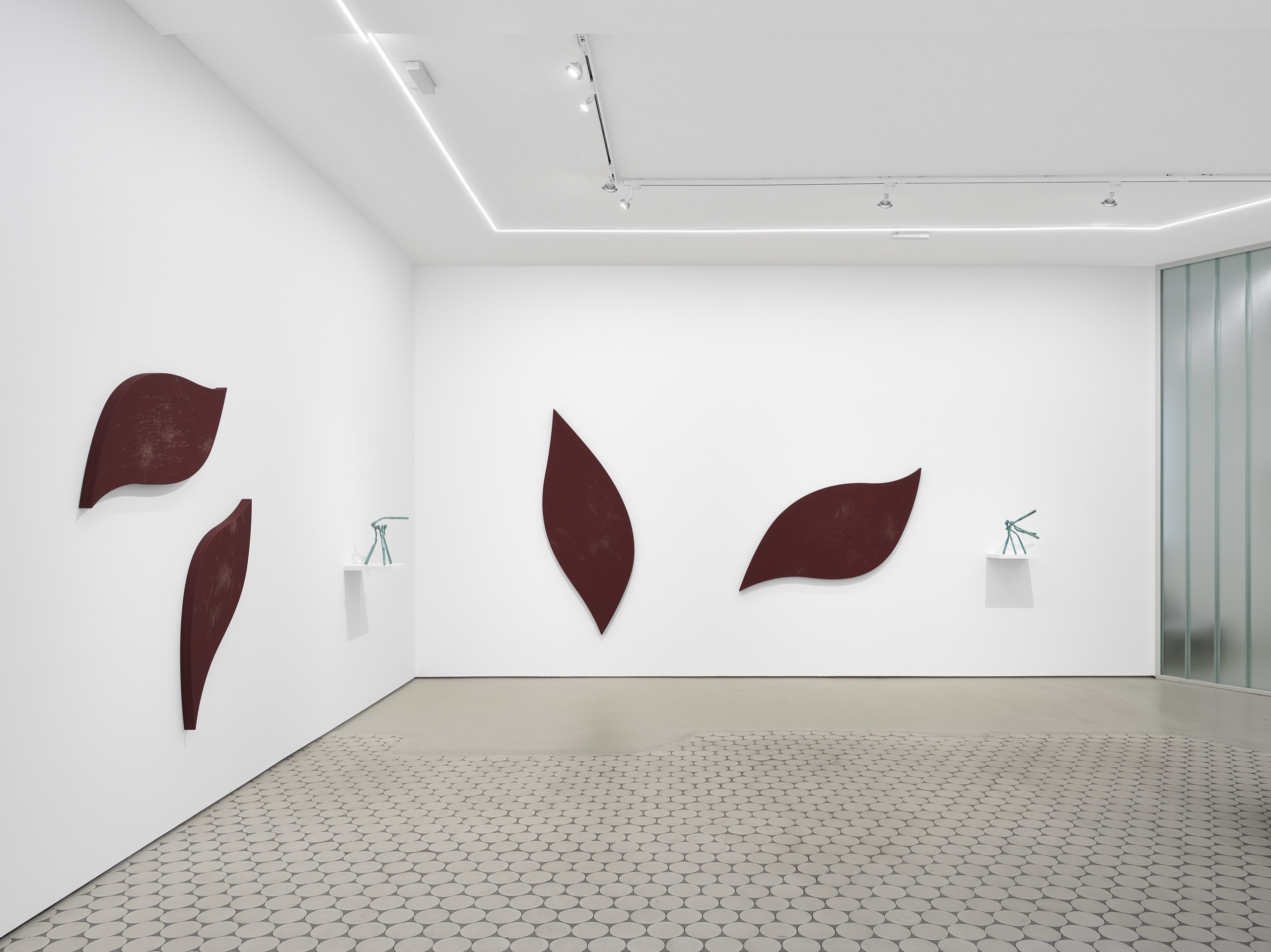 Installation view with curved oxblood leaf-shaped wall reliefs and small bronze sculptures on white shelves